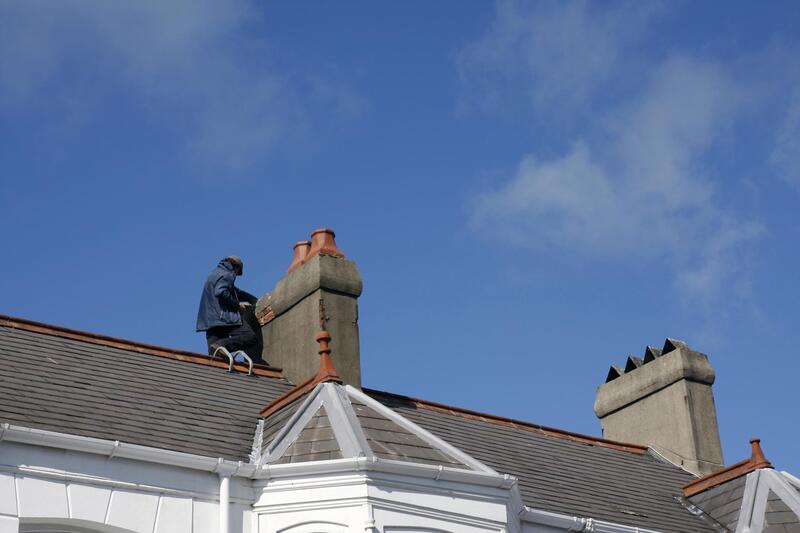 a man on the roof repairing the flashing around the chimney in Fredericton, NB